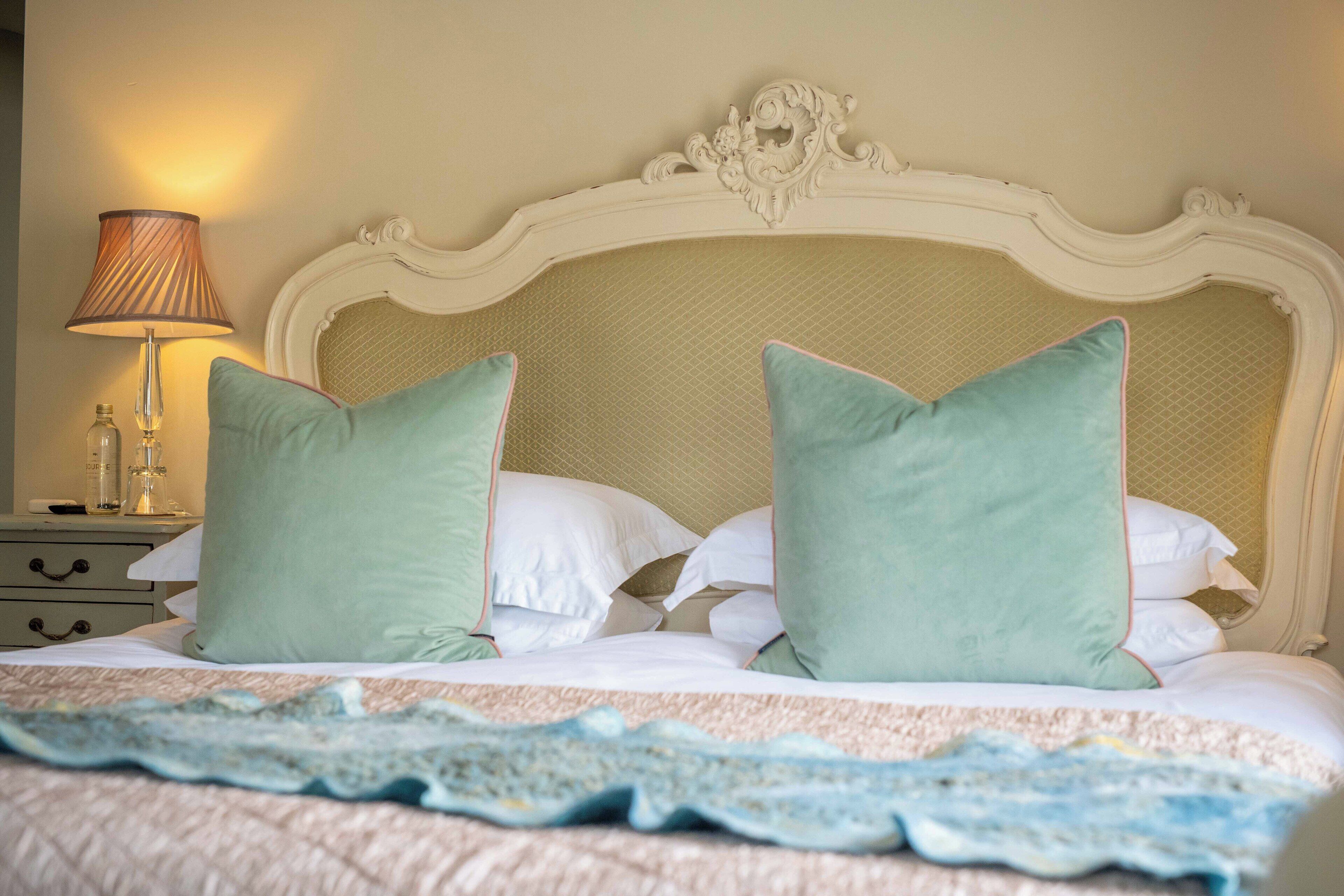 A neatly made bed with a patterned bedspread, a decorative headboard, and a bedside table with a lamp and a bottle.