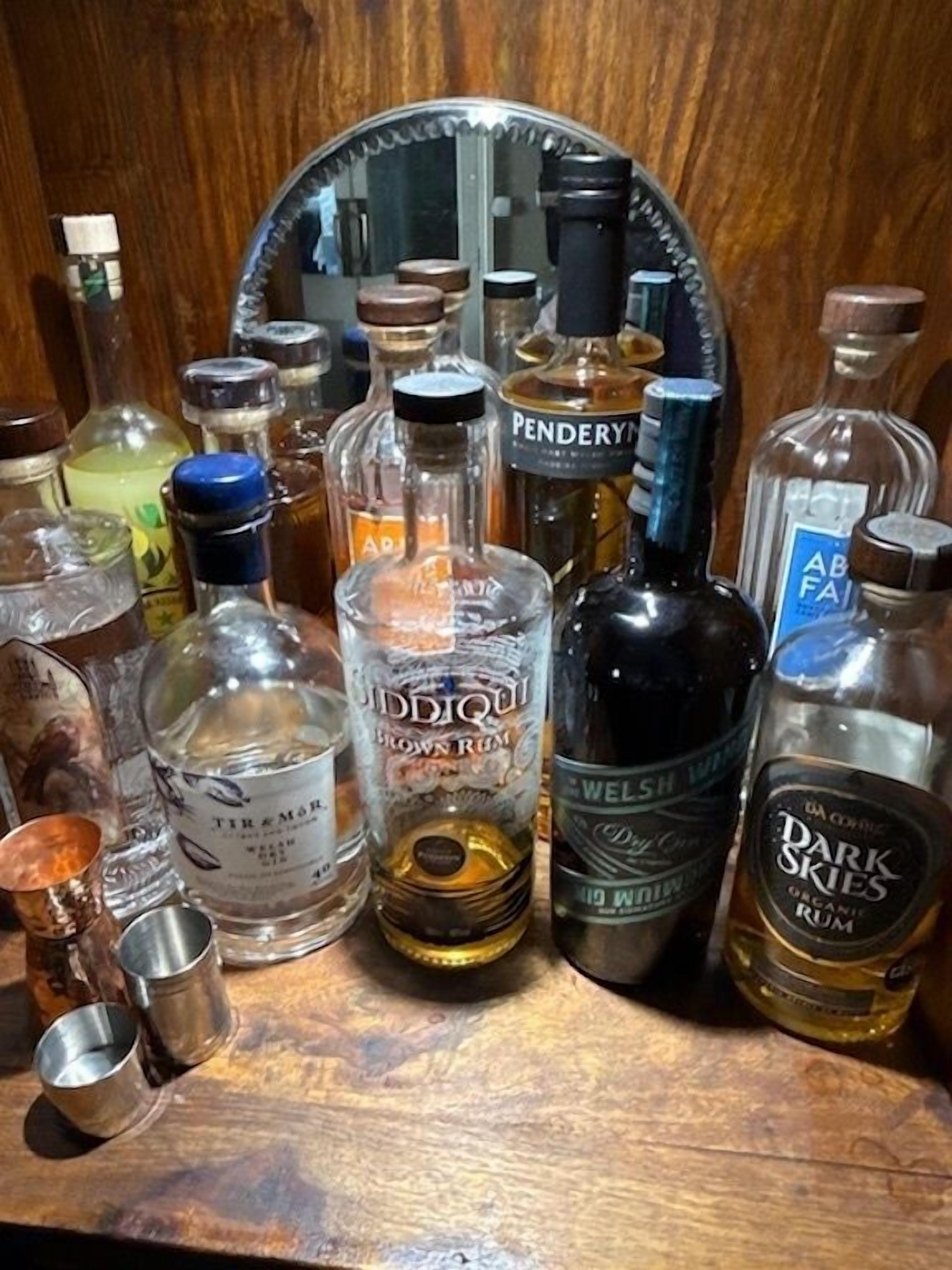 Varias botellas de licor sobre una superficie de madera, con un espejo al fondo.