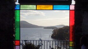 Une vue à travers un vitrail d’un lac paisible où flottent des bateaux, le tout entouré d’arbres et de collines.