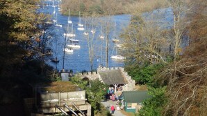 Une vue sur la rivière, avec des bateaux, un pont de pierre et un petit bâtiment où se trouvent des personnes.
