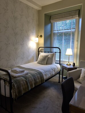 A bedroom with a bed, a nightstand, a chair, and a window with blinds. - Haisthorpe House (Windermere)