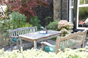 A wooden table with benches in a garden area with stone walls and plants. - Haisthorpe House (Windermere)