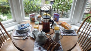 Une table de petit-déjeuner dressée avec des assiettes, une théière, un pichet et des boîtes de céréales.