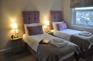 A hotel room with two beds, each with a headboard, bedside lamps, and a window. - Haisthorpe House (Windermere)