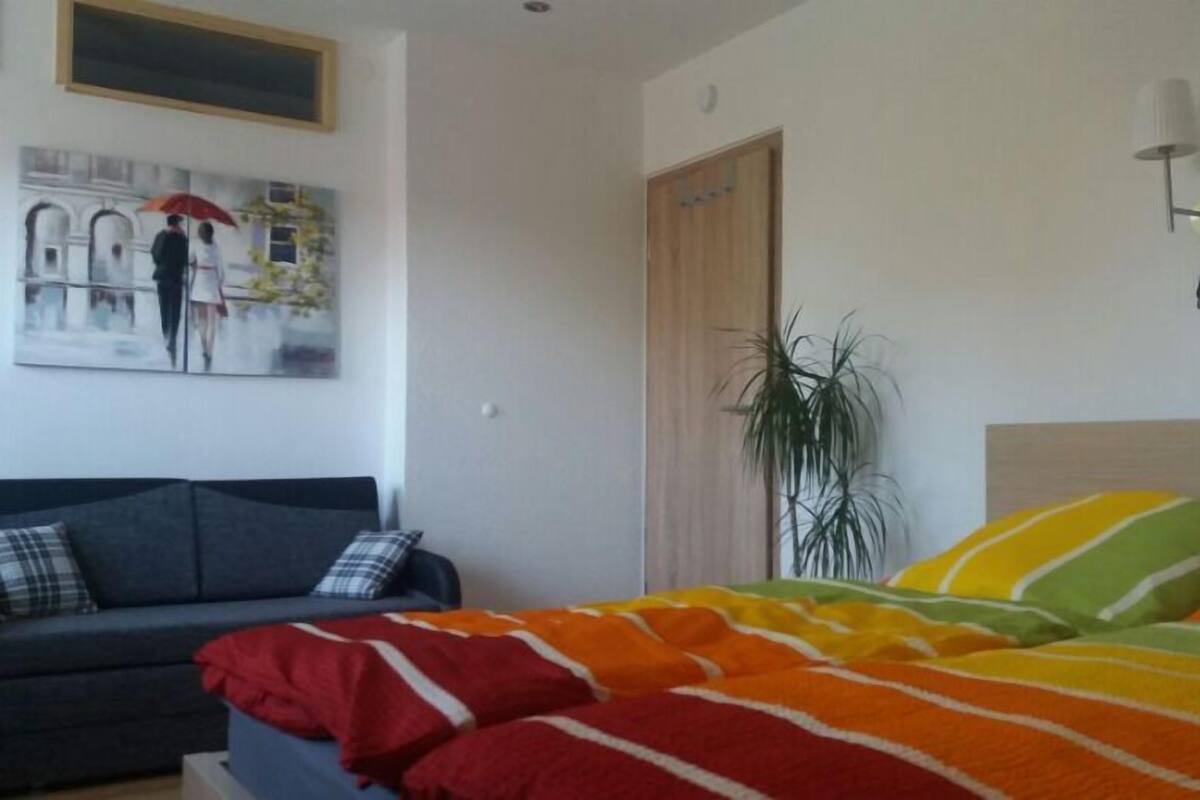 A hotel room with a bed, a sofa, a painting, a plant, and a wall-mounted lamp.