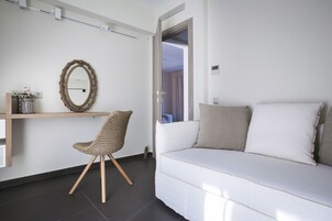 Un salon moderne avec un canapé blanc, un fauteuil en osier, une étagère en bois ornée d’objets décoratifs et un miroir au mur.