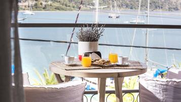 A balcony with a table set for breakfast, overlooking a body of water with boats.