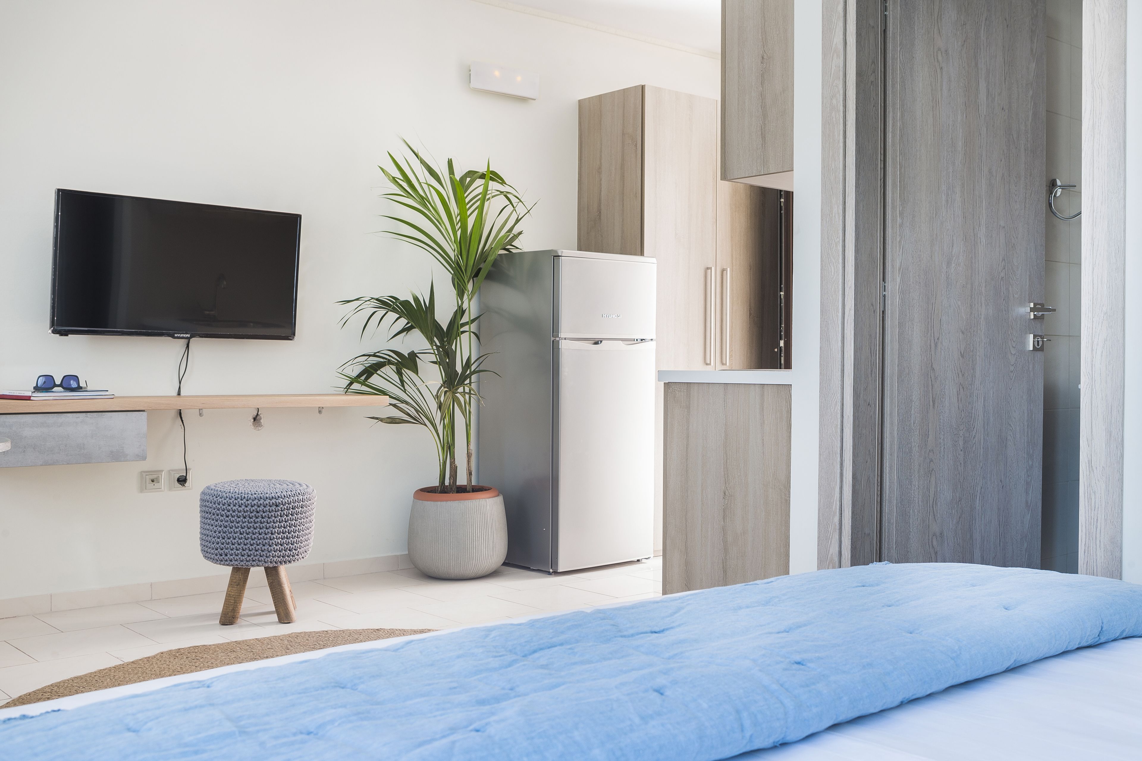 Un dormitorio moderno con cama, televisión montada en la pared, refrigerador y una planta en maceta.