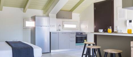 A modern kitchen with a refrigerator, microwave, and oven. There is a bar counter with stools and a bed with a blanket.