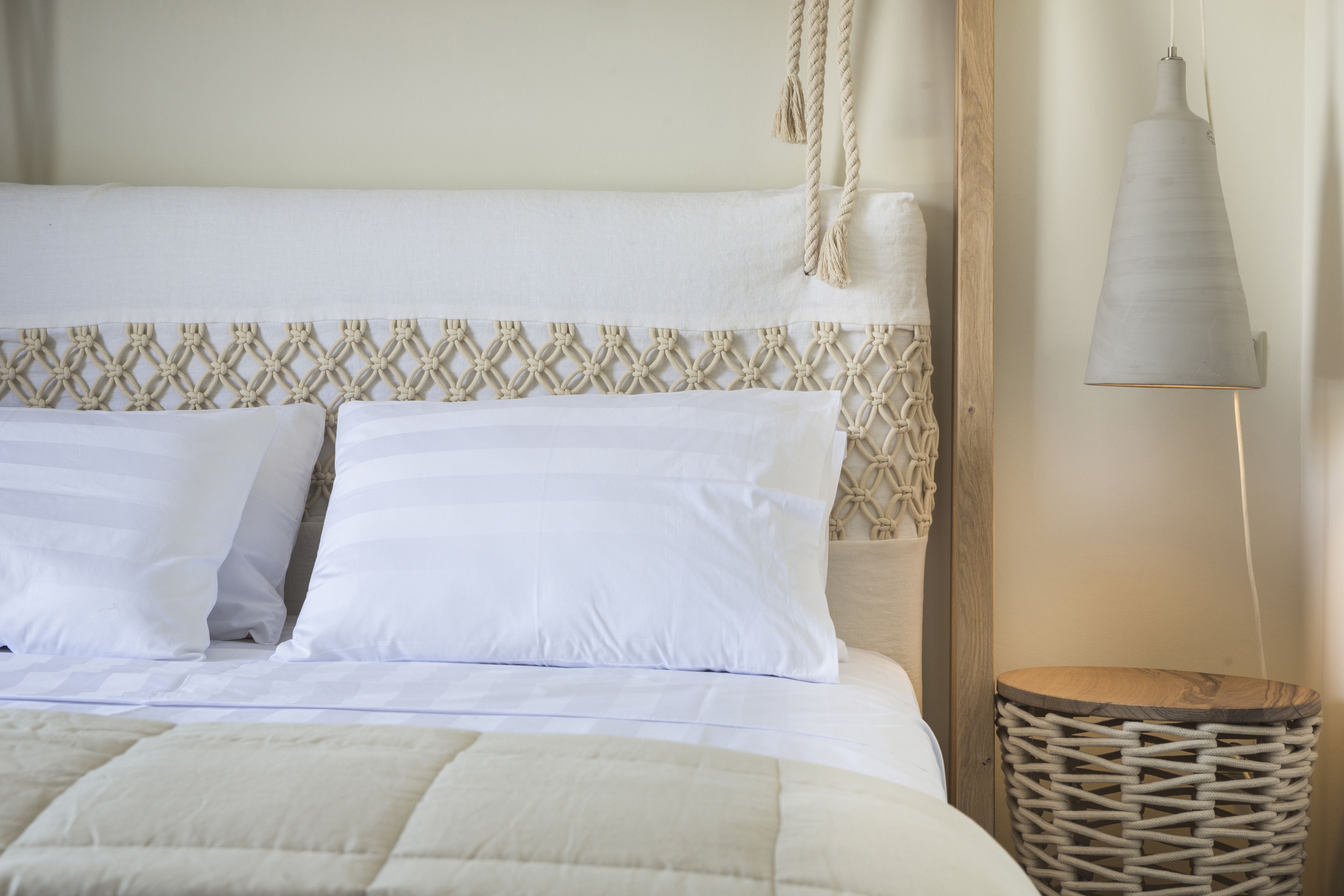 Un lit bien fait, avec une tête de lit à motifs, une lampe de chevet et une table de chevet en osier.