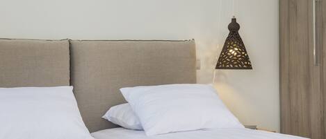 A neatly made bed with white linens and a beige headboard.