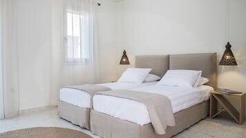 Una cama doble con cabecera, dos mesitas de noche, una ventana con cortinas traslúcidas y una lámpara de pie.