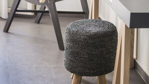 A modern room with a dark wooden table, two white vases with dried flowers, a woven chair with a beige cushion, and a round woven stool. - Argostoli Marina Suites (Kefalonia)
