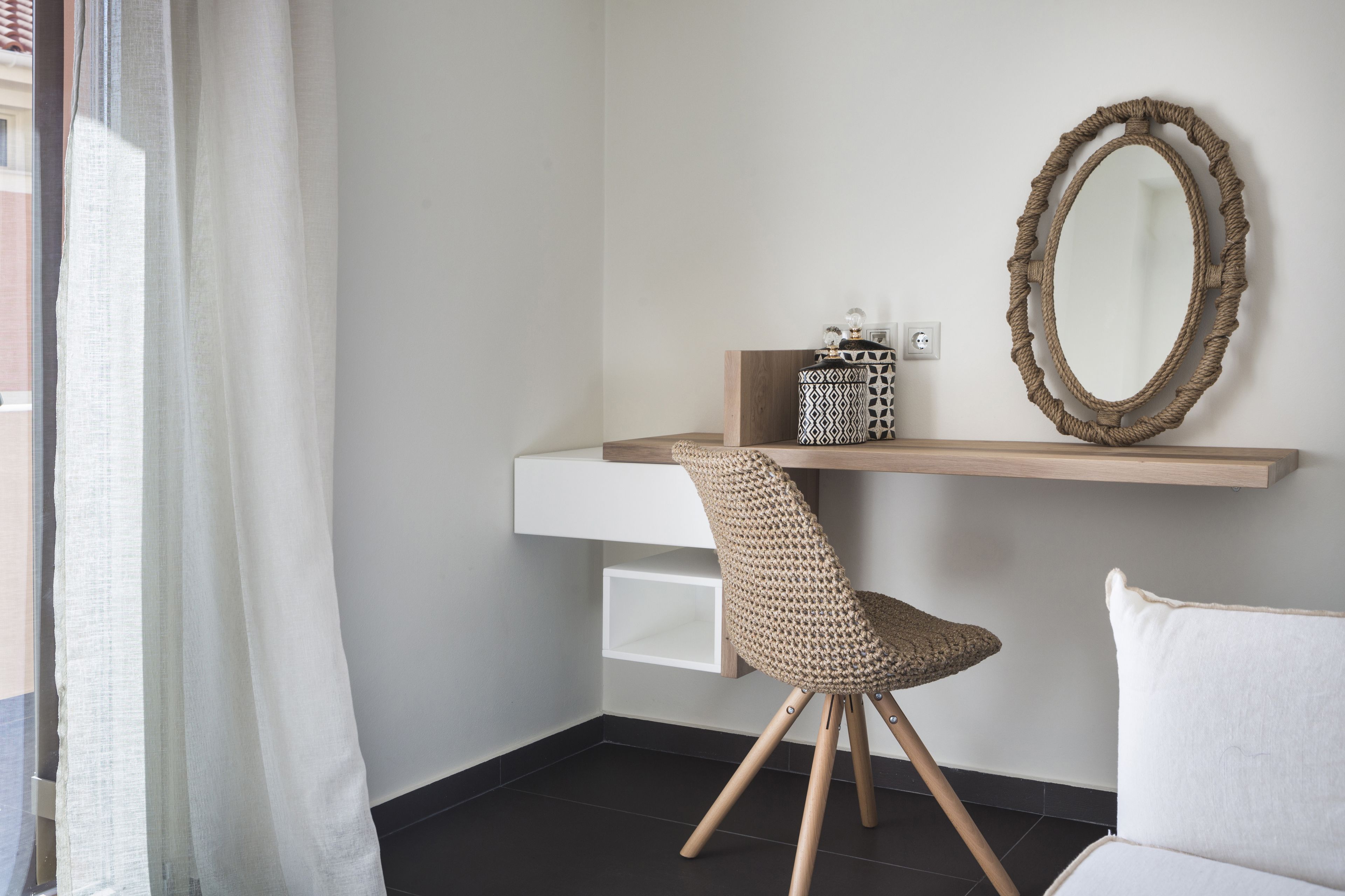 Una habitación moderna con un escritorio blanco, una silla tejida, un espejo y un sofá blanco.