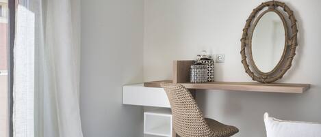 Una habitación moderna con un escritorio blanco, una silla tejida, un espejo y un sofá blanco.