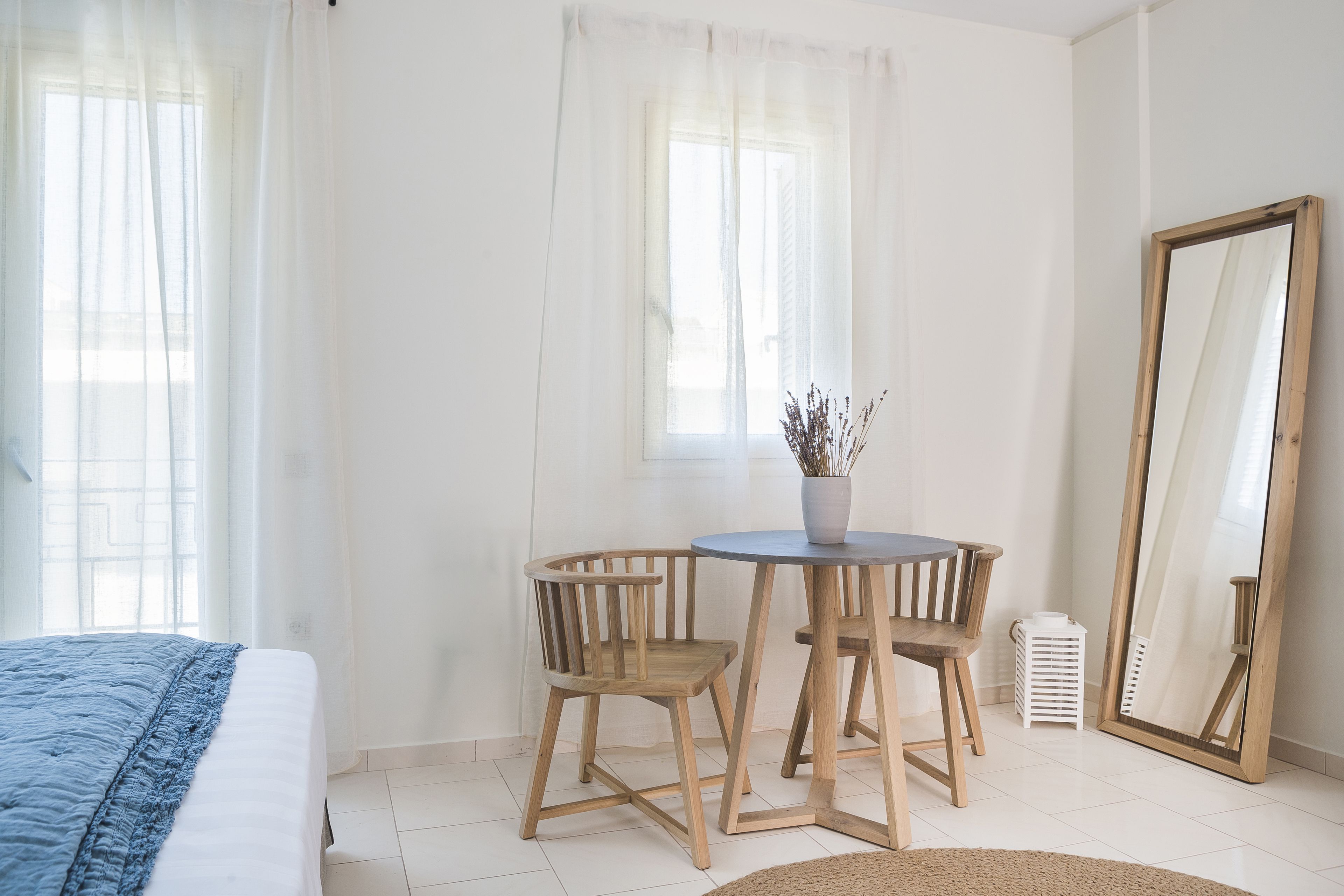 Un dormitorio con cama, una mesa de madera con sillas, un espejo y una ventana con cortinas translúcidas.