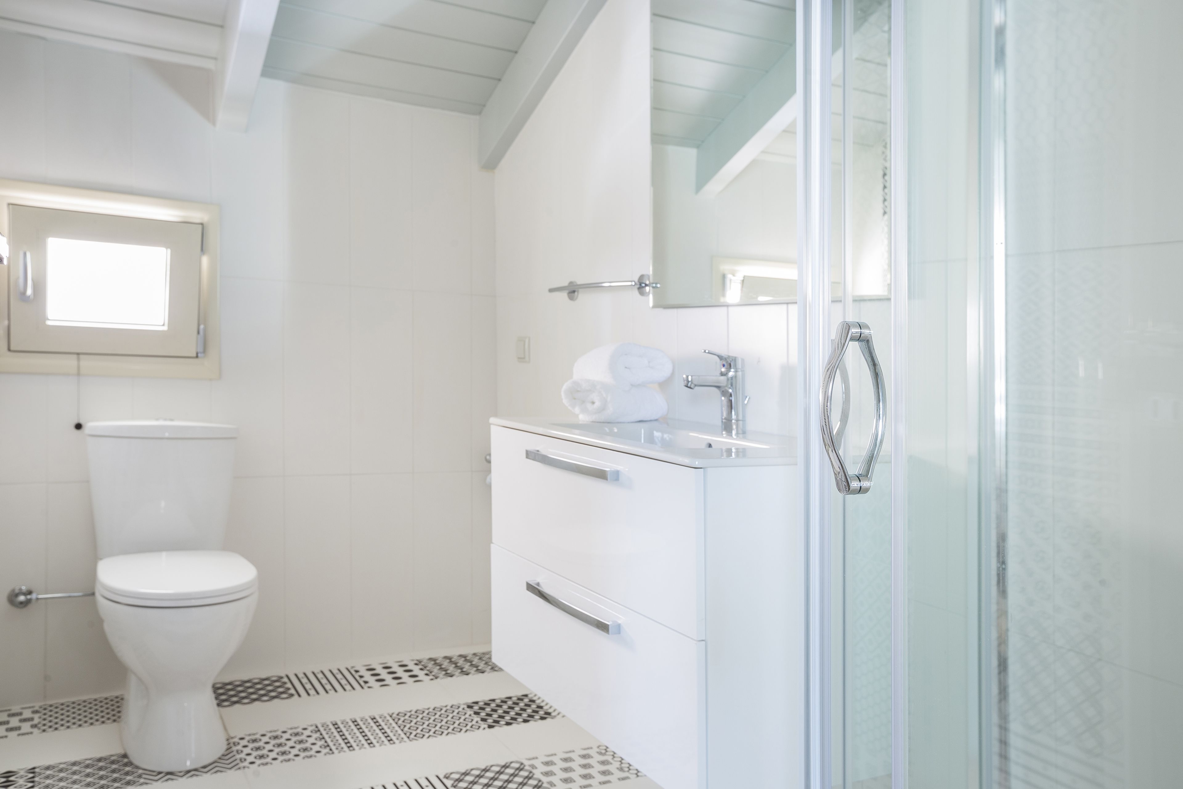 A bathroom with a toilet, a sink with a mirror, and a shower area.