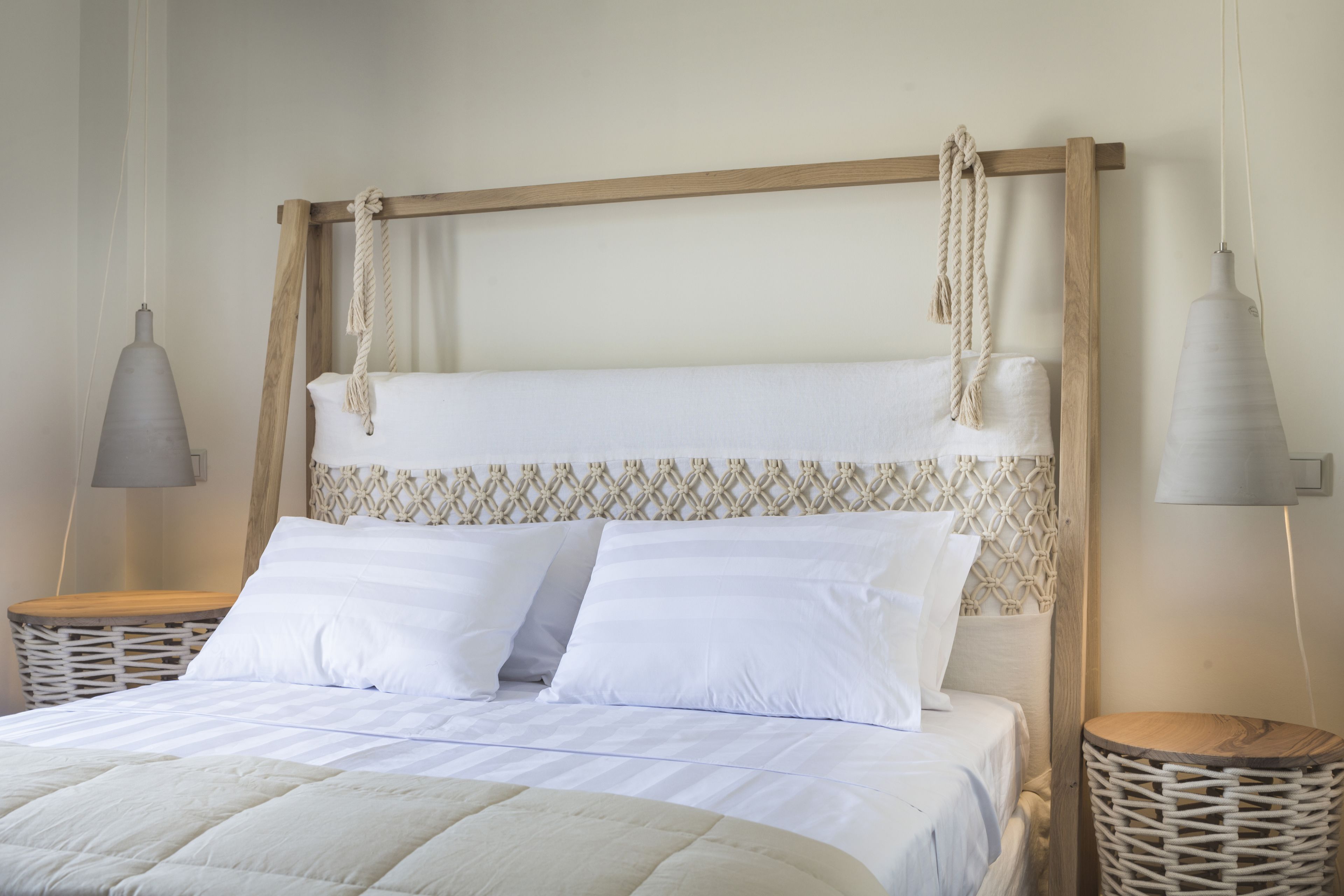 A neatly made bed with white linens and a wooden headboard with rope details. There are two bedside tables with lamps and a woven basket.