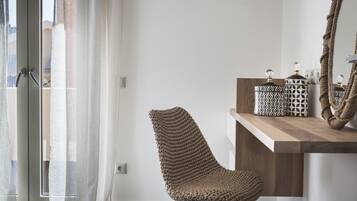 Een moderne kamer met een groot raam, een geweven stoel, een houten bijzettafeltje met decoratieve objecten en een spiegel.