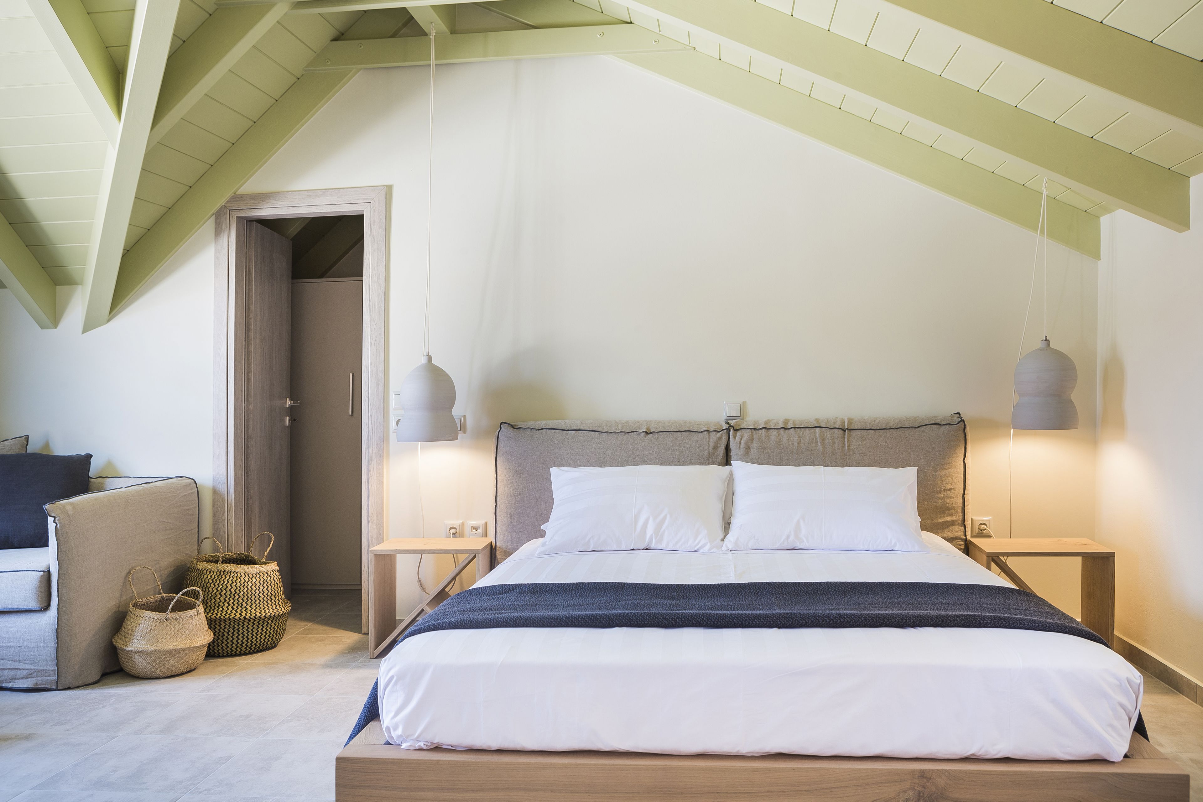 A bedroom with a wooden bed, two bedside lamps, a nightstand, a woven basket, and a door leading to another room.