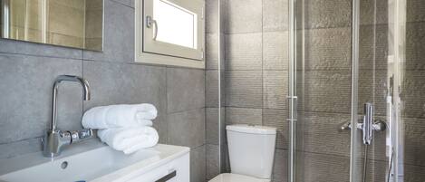 A modern bathroom with a white sink, a toilet, and a glass-enclosed shower.