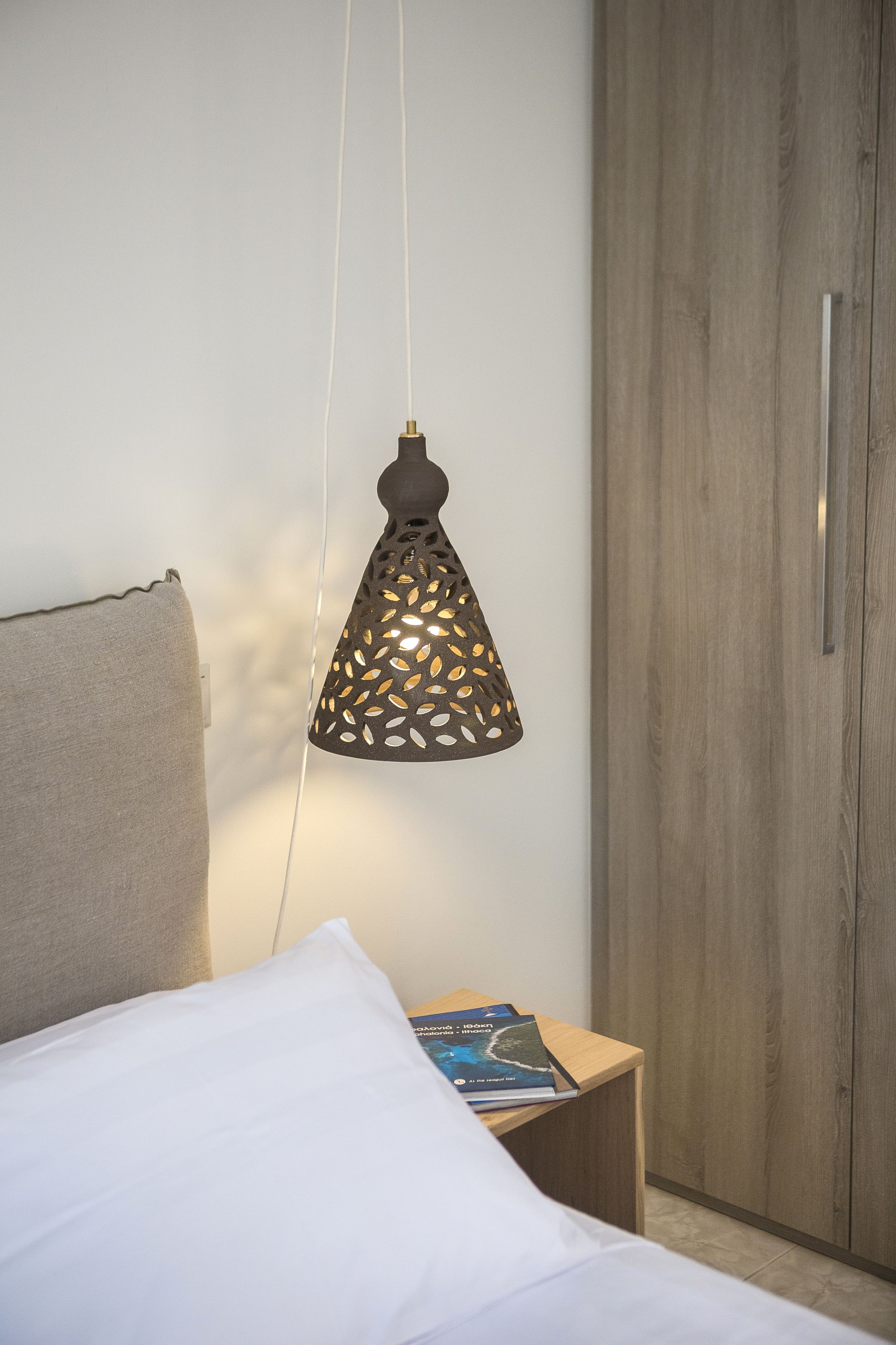 Un dormitorio con cama, mesita de noche con un libro, lámpara colgante y armario.