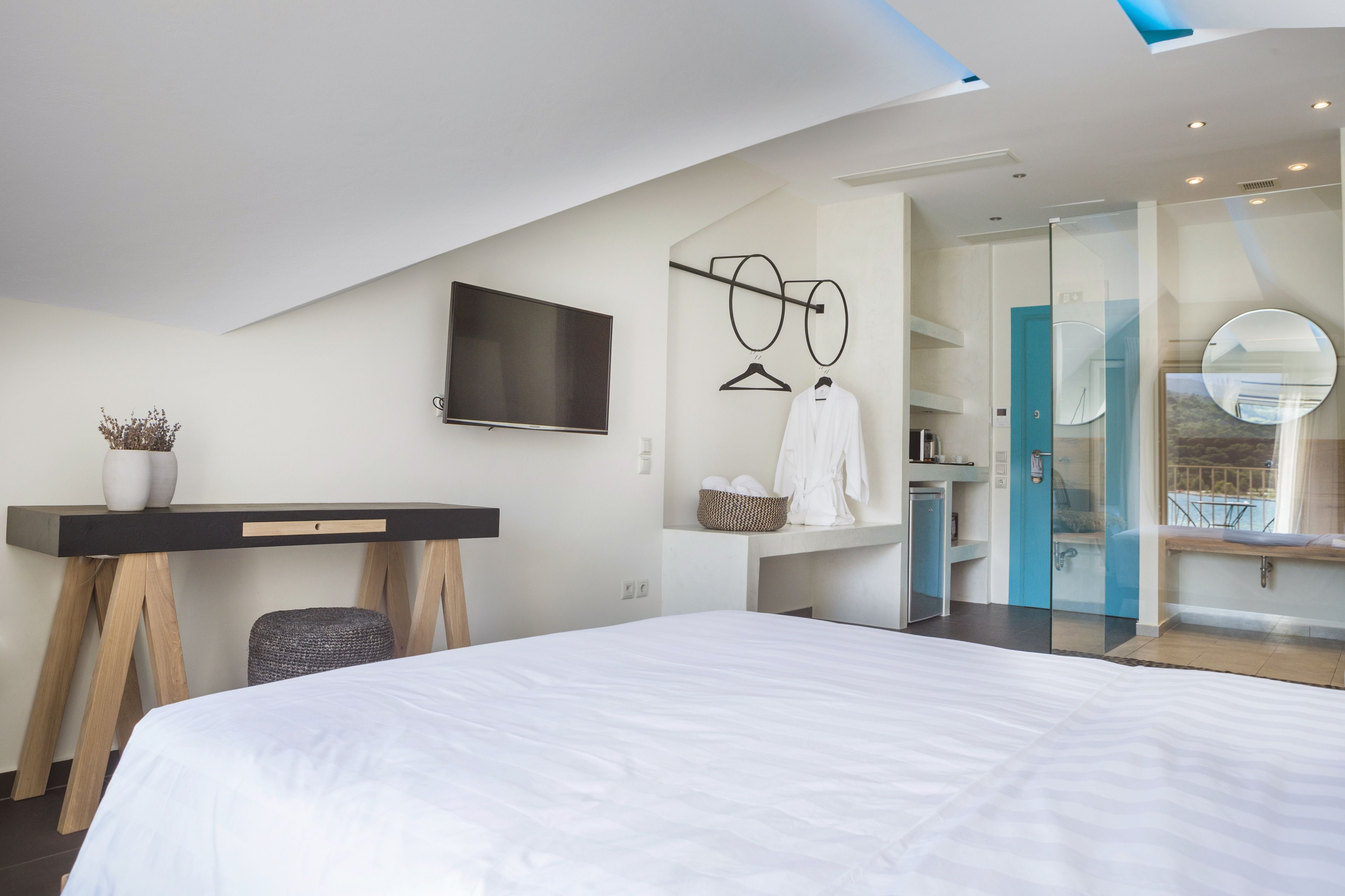 Une chambre d’hôtel moderne dotée d’un grand lit, d’un bureau avec un téléviseur à écran plat, d’une robe de chambre et d’une salle de bain avec une douche en verre.