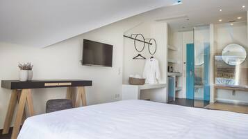 Habitación de hotel moderna con una cama grande, un escritorio con televisor de pantalla plana, bata colgada y baño con ducha de vidrio.