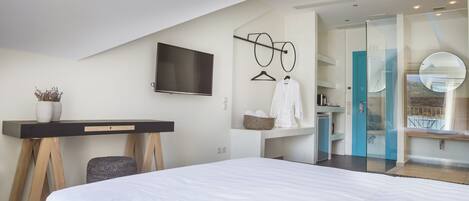 Une chambre d’hôtel moderne dotée d’un grand lit, d’un bureau avec un téléviseur à écran plat, d’une robe de chambre et d’une salle de bain avec une douche en verre.