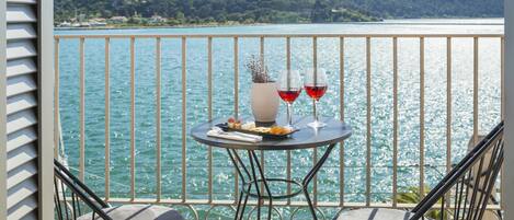 A balcony with a table set for two, overlooking a lake with mountains in the background.