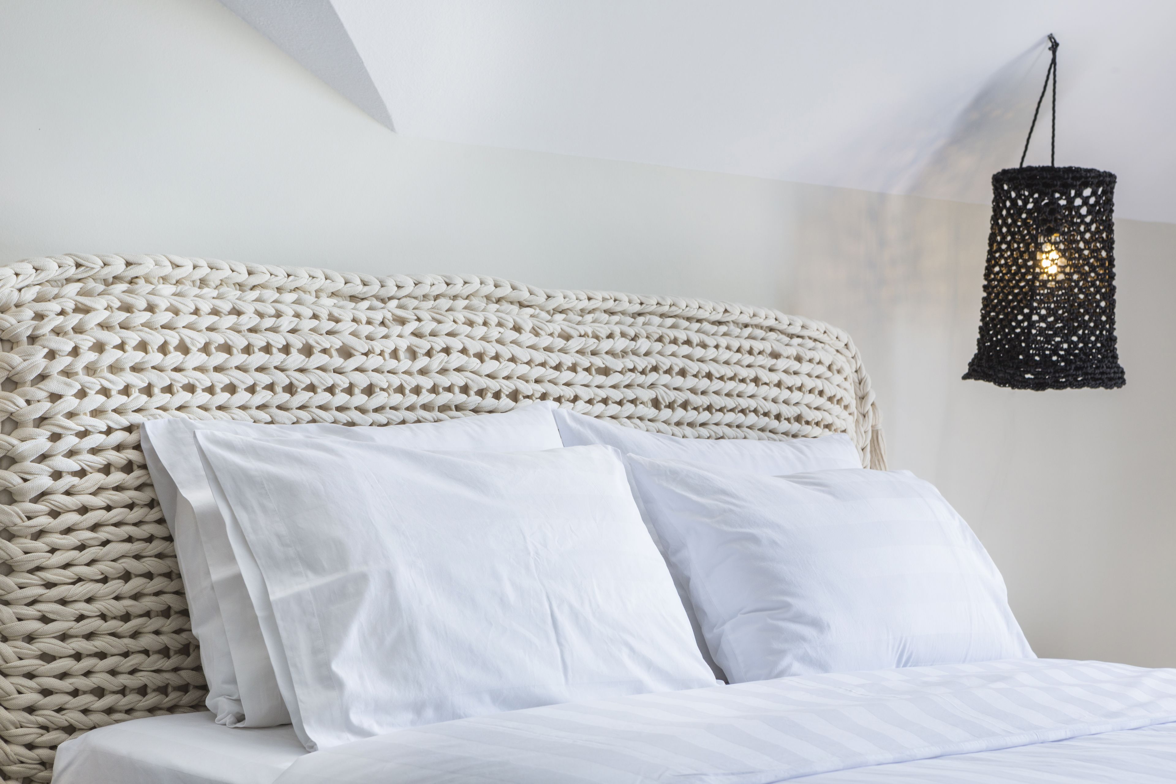 A bed with white linens and a woven headboard.