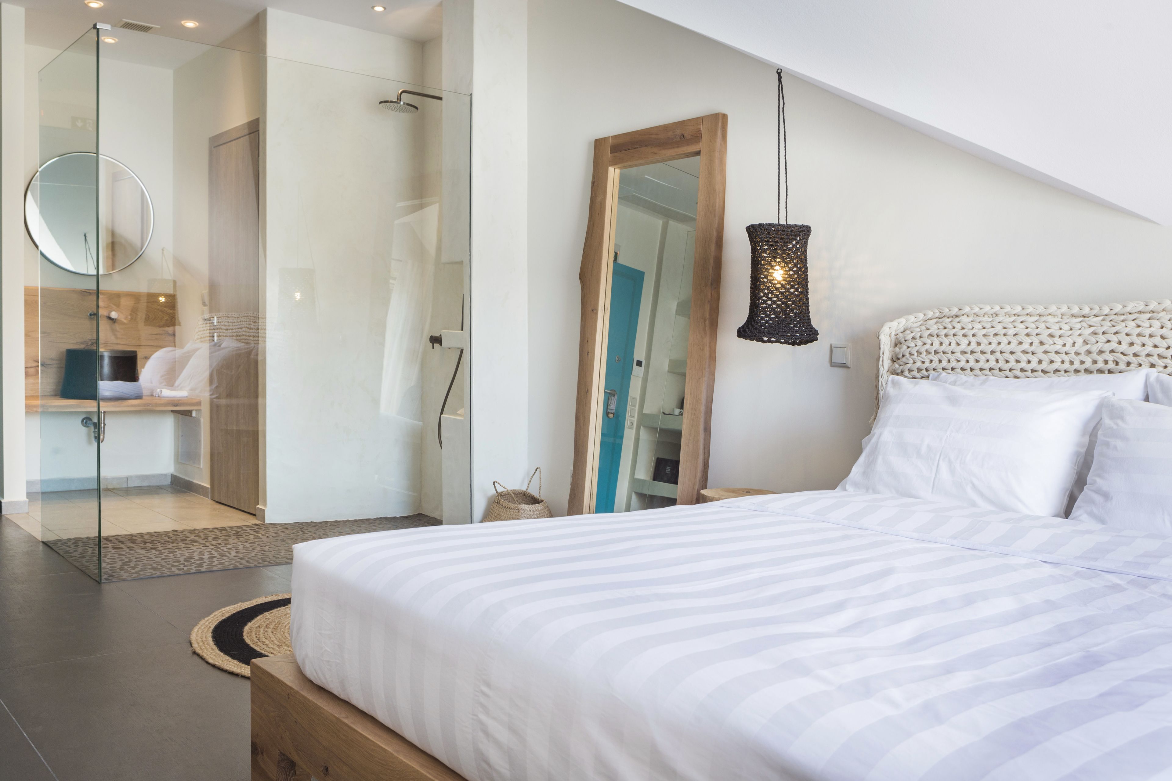 A modern bedroom with a large bed, a mirror, a hanging light fixture, and a walk-in closet.