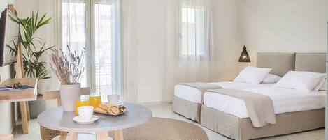 A modern hotel room with a bed, a dining area with a table and chairs, and a large window with curtains.