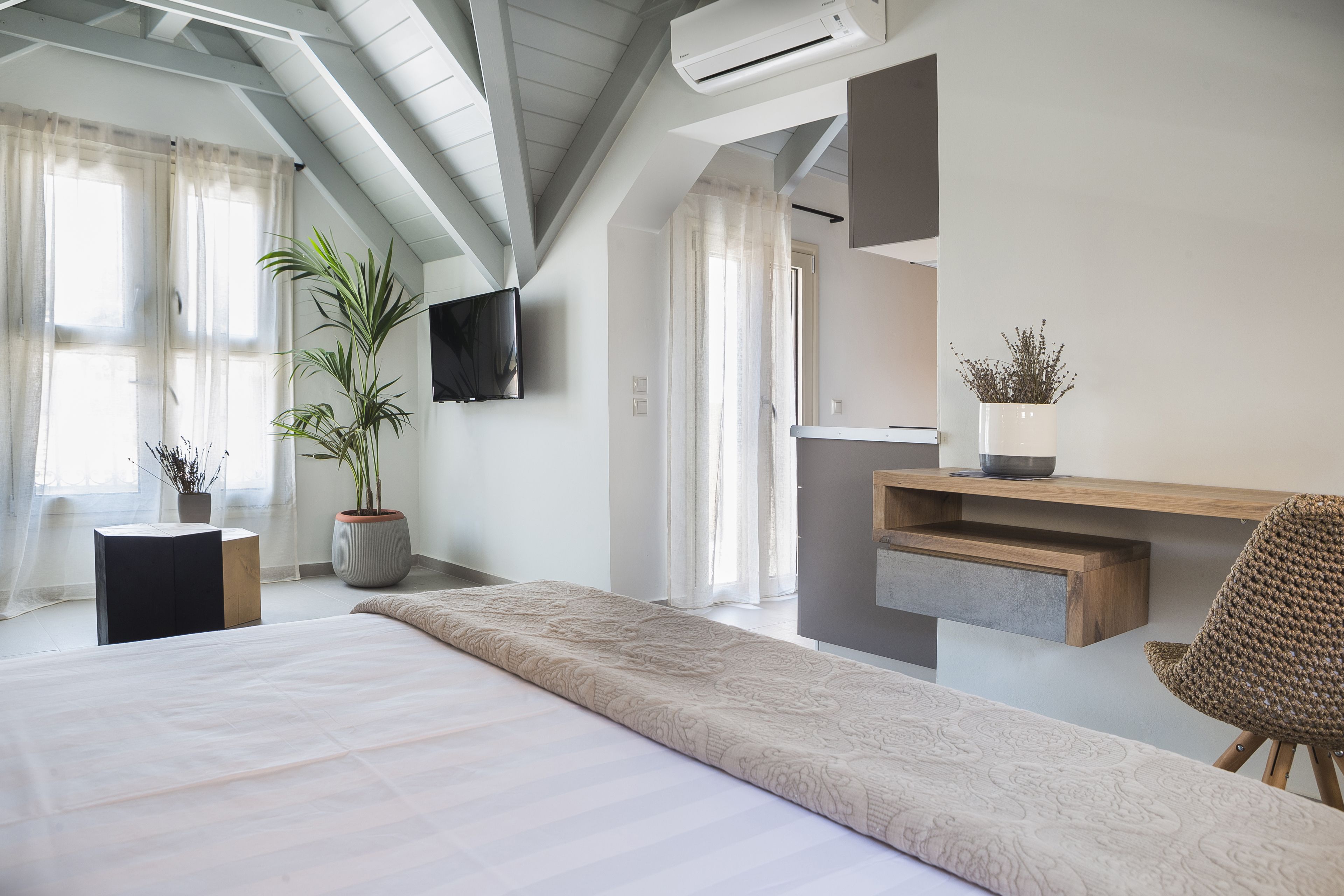 A modern bedroom with a large bed, a wooden desk, a chair, a potted plant, and a mounted TV.