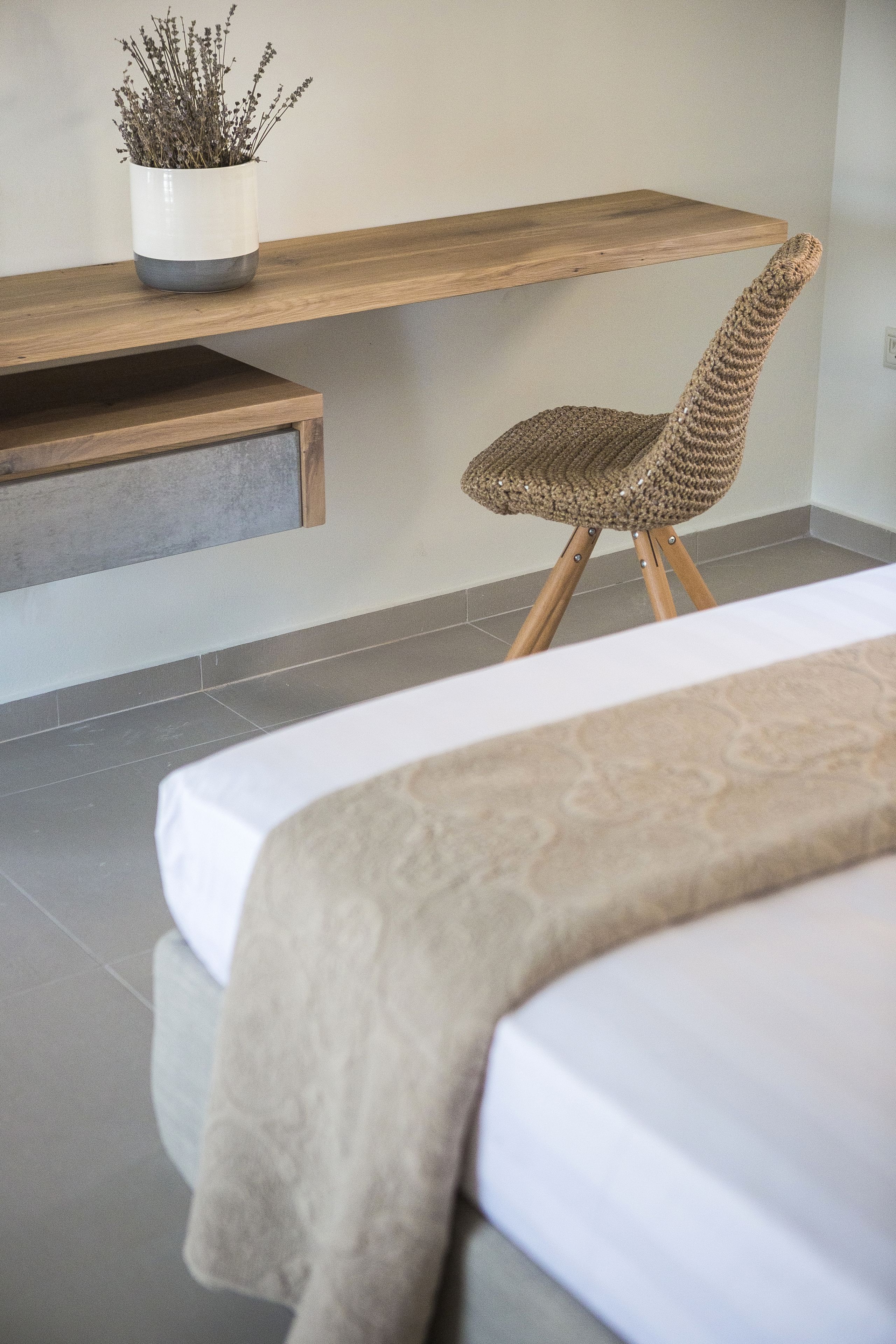 A modern bedroom with a bed, a woven chair, a wooden shelf, and a potted plant.