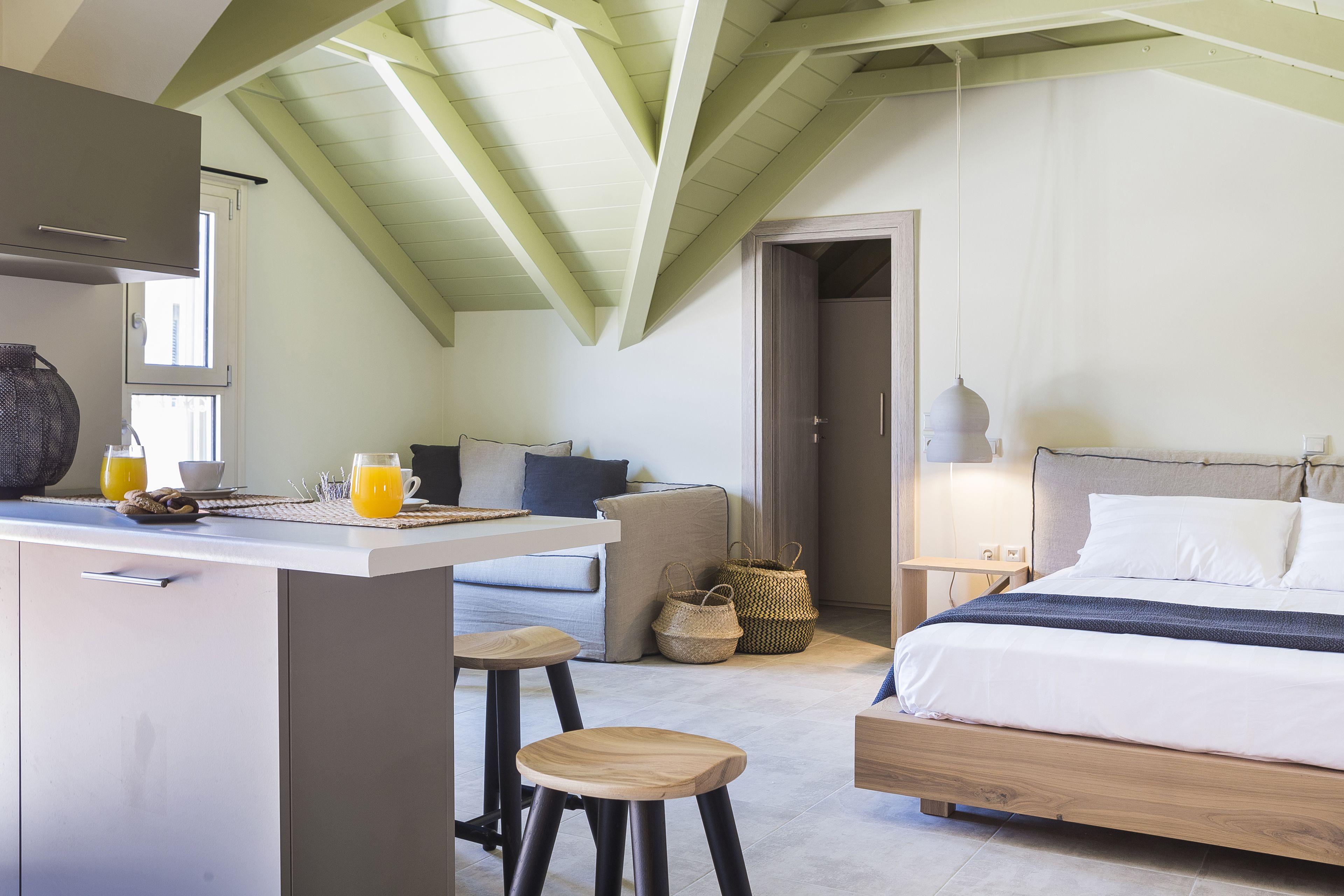 A bedroom with a bed, bedside table, and a small kitchenette area with stools.