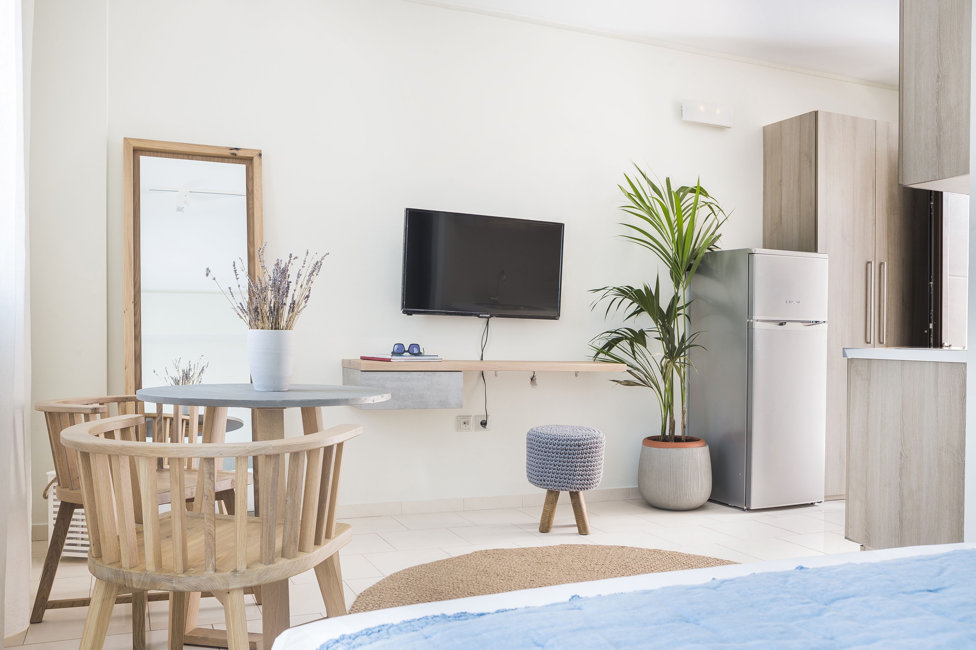 A modern kitchen with a flat-screen TV, wooden cabinets, a refrigerator, and a dining area with a round table and chairs.