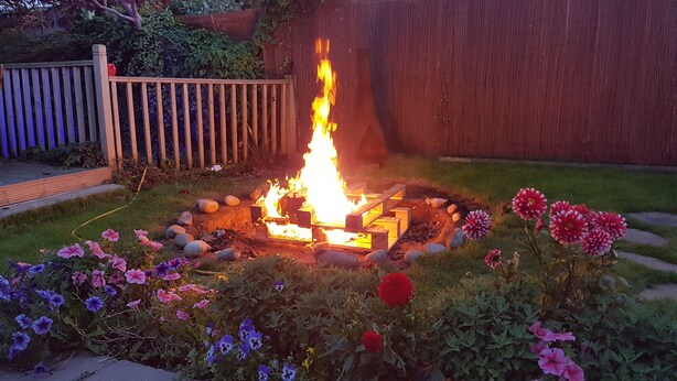 A fire pit surrounded by rocks and flowers in a garden. - John Wayne Lodge (Peacehaven)