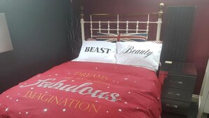 A bed with a red cover and pillows with the words "BEAST" and "Beauty". - John Wayne Lodge (Peacehaven)