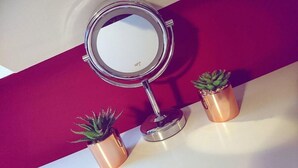A round mirror with a metallic frame, two potted plants, and a red and white background. - John Wayne Lodge (Peacehaven)