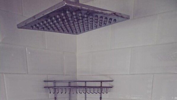 Un cabezal de ducha con múltiples boquillas, un perchero metálico con ganchos y una pared con azulejos.