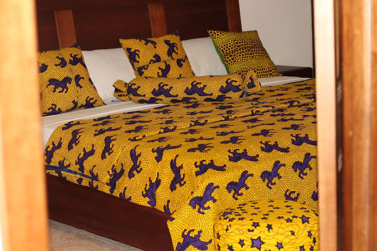 A bed with a patterned bedspread and pillows, a wooden headboard, and a white wall in the background.