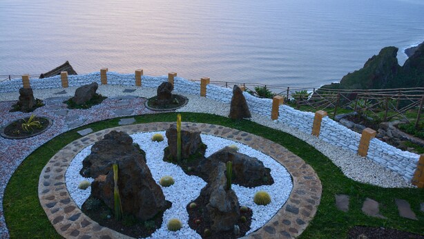 A landscaped garden with a circular stone pathway, rock formations, and a view of the ocean. - Hotel Jardim Atlantico (Calheta)