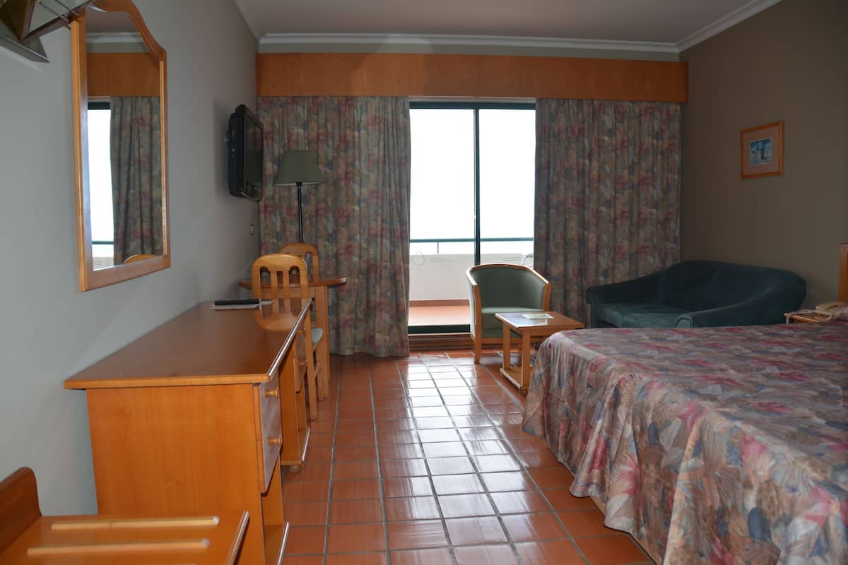 A hotel room with a bed, a desk, a chair, a television, and a balcony with curtains.