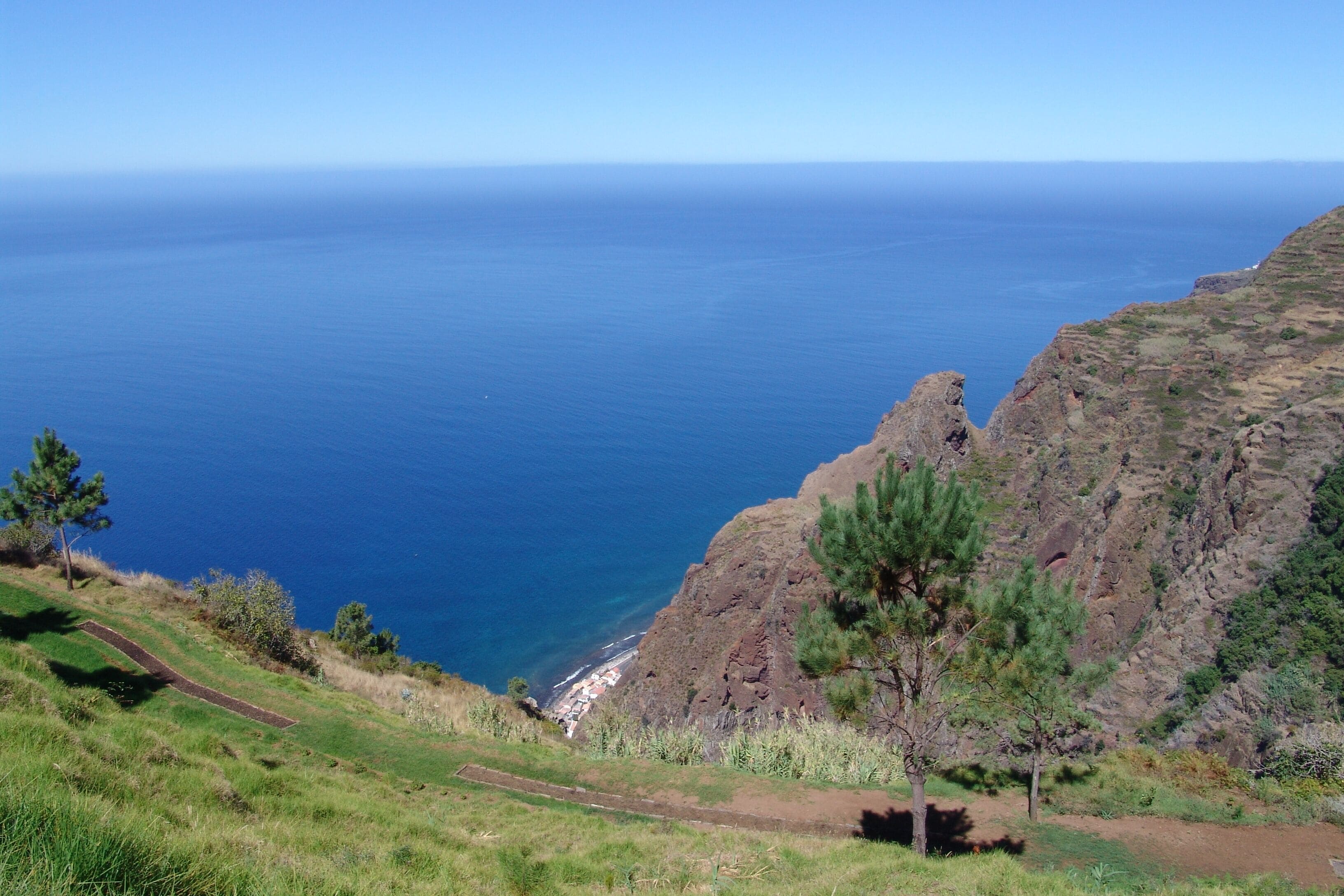 A coastal landscape with a clear view of the sea, a rocky cliff, and a grassy area with a path.