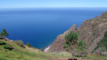 A coastal landscape with a clear view of the sea, a rocky cliff, and a grassy area with a path.