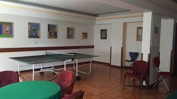 A room with a ping pong table, chairs, and framed pictures on the wall.