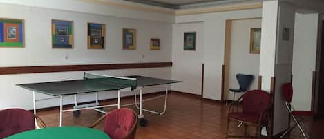 A room with a ping pong table, chairs, and framed pictures on the wall.