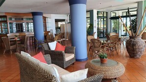 A spacious lobby with wicker furniture, large pillars, and a central round table with a potted plant. - Hotel Jardim Atlantico (Calheta)
