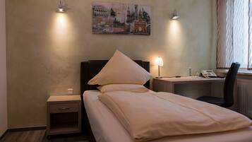 A hotel room with a bed, bedside tables, a desk, and a lamp.